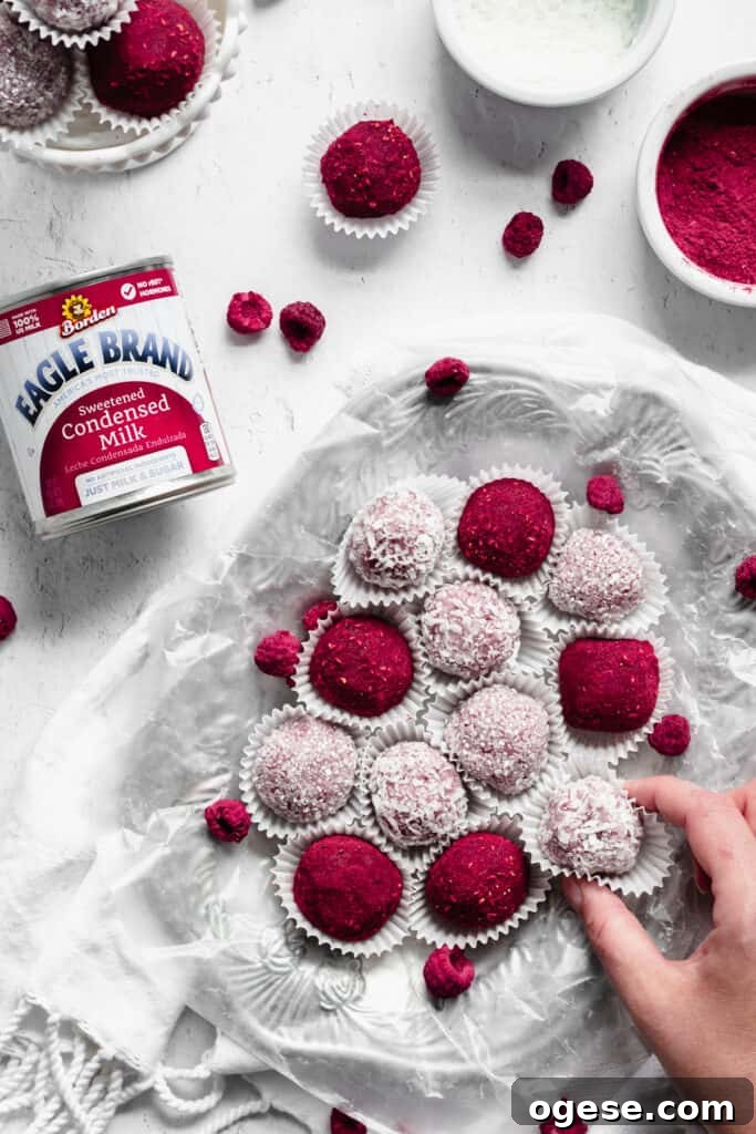Overhead shot of a platter of raspberry brigadeiros. A hand reaches in to remove one.