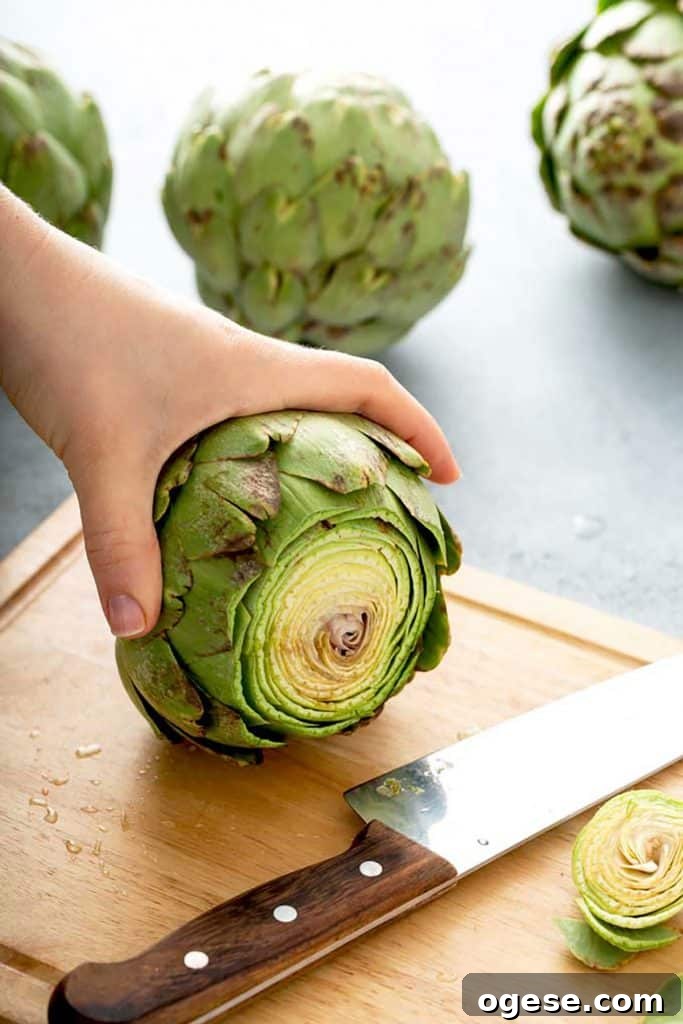 How to Cook Artichokes: Steamed and Roasted Methods 6 holding an artichoke with the stem cut off on a cutting board