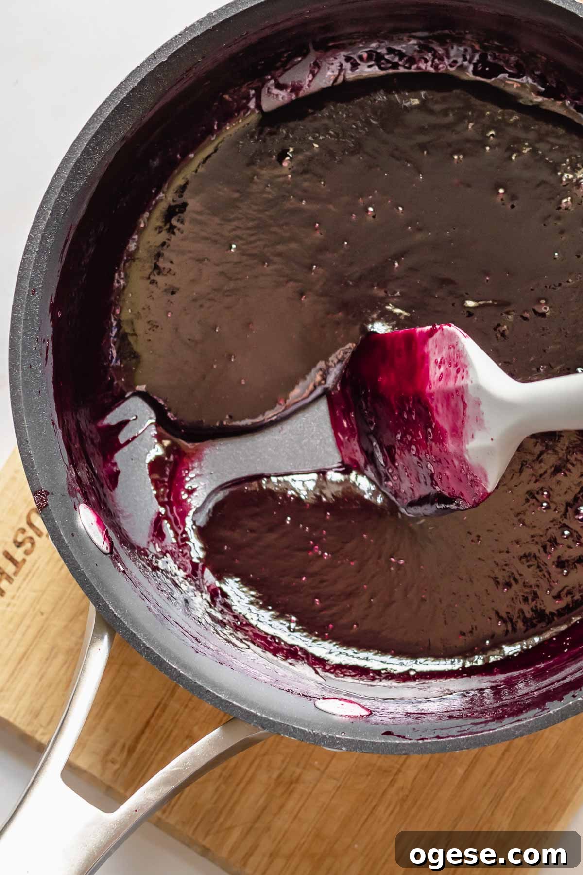 A spatula drags reduced blackberry puree in a pot.