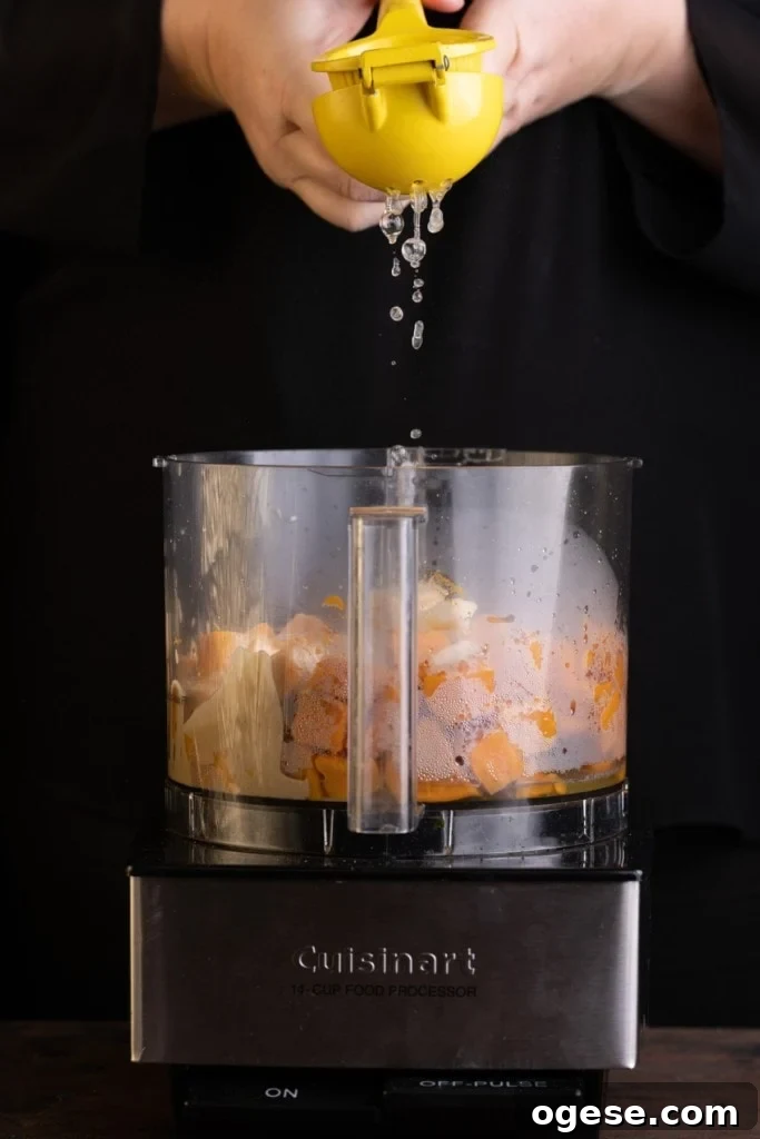 Adding lemon juice to food processor with boiled sweet potato, garlic, tahini, salt, and pepper. 