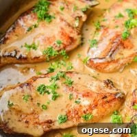 A close up of a skillet of chicken breasts in a creamy sauce, garnished with parsley.