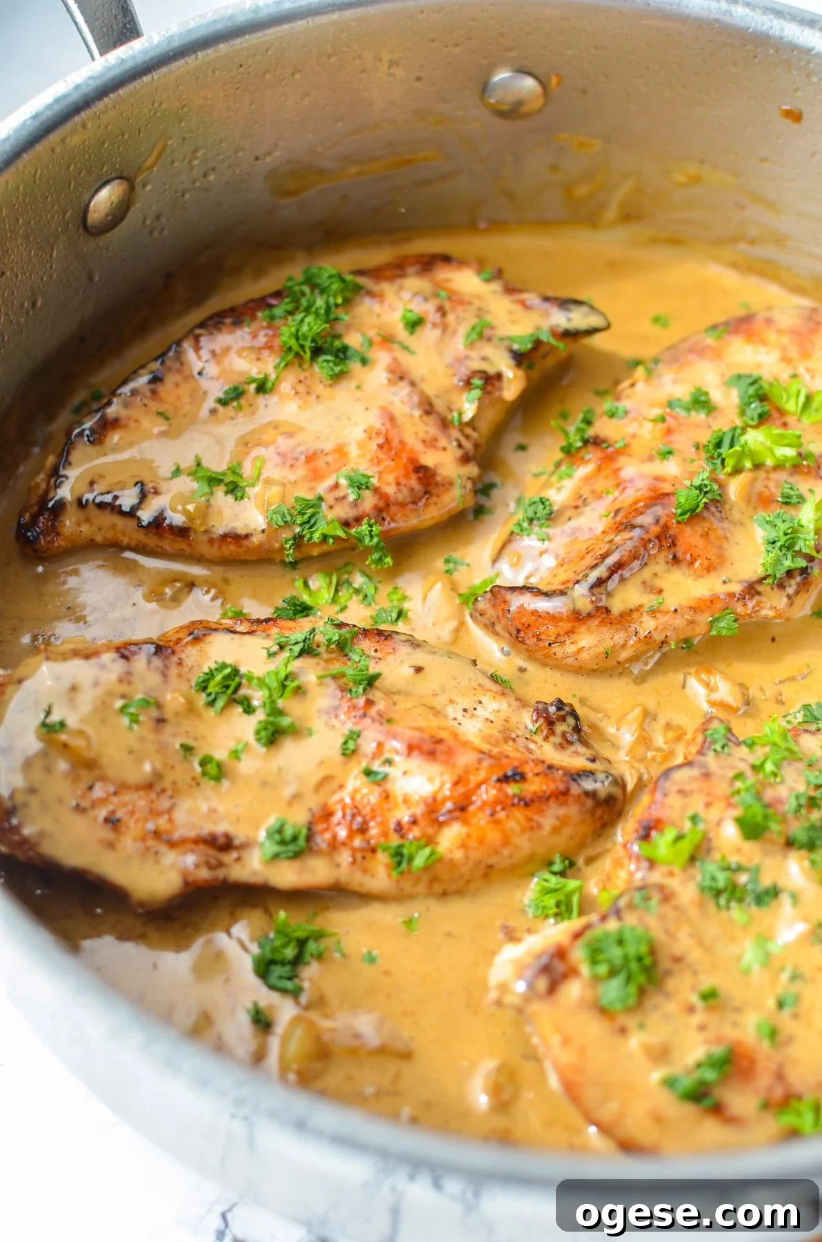 A skillet with chicken breasts and garlic sauce, sprinkled with parsley.