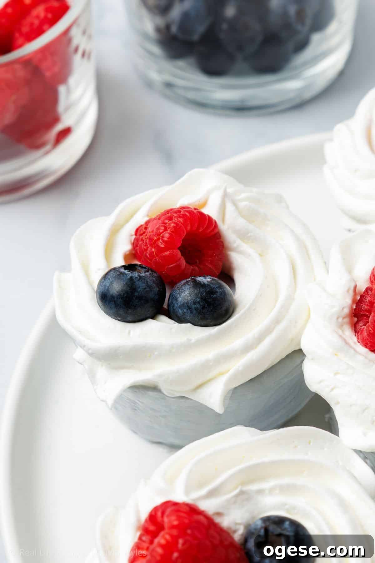 Close-up of a no-bake mini cheesecake swirled with whipped cream and topped with a raspberry and two blueberries