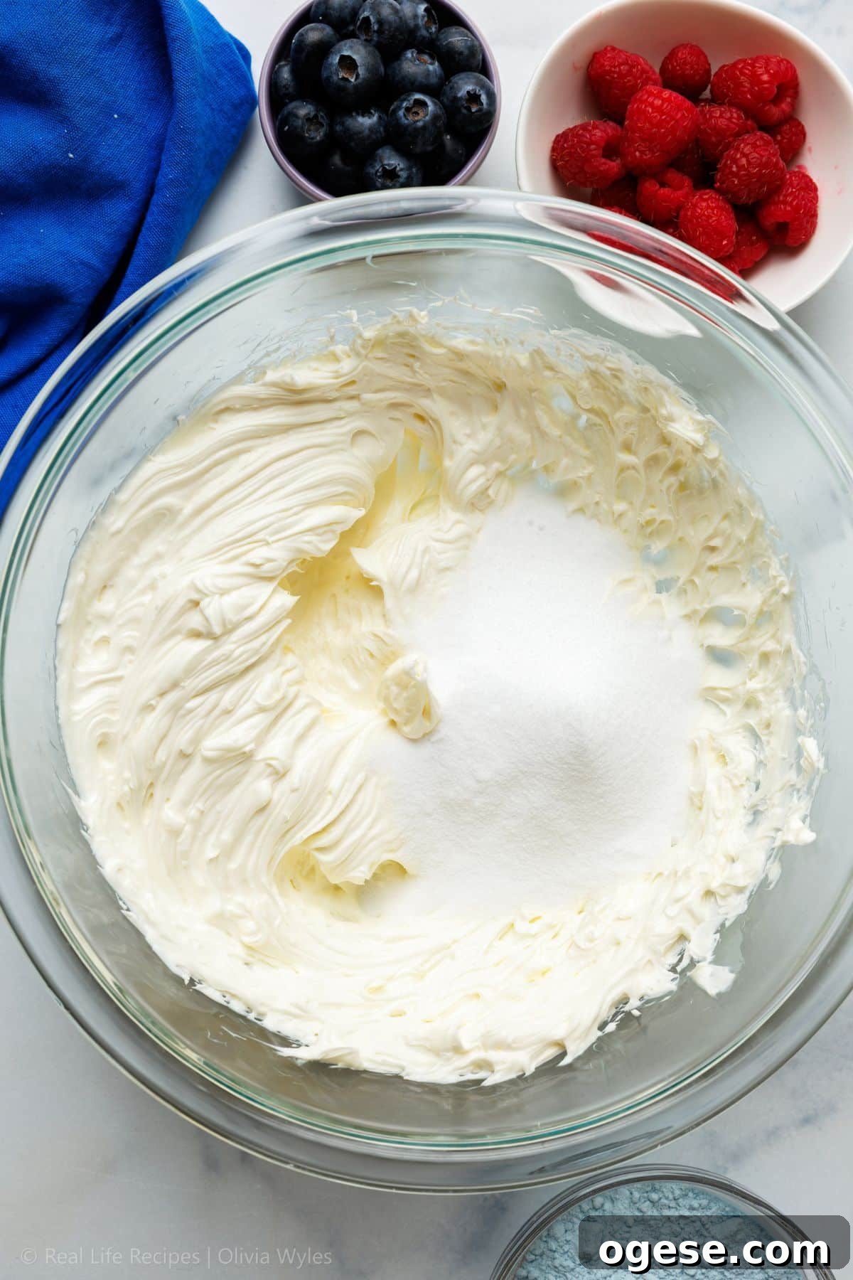 Powdered sweetener being added to the whipped cream cheese in a glass bowl