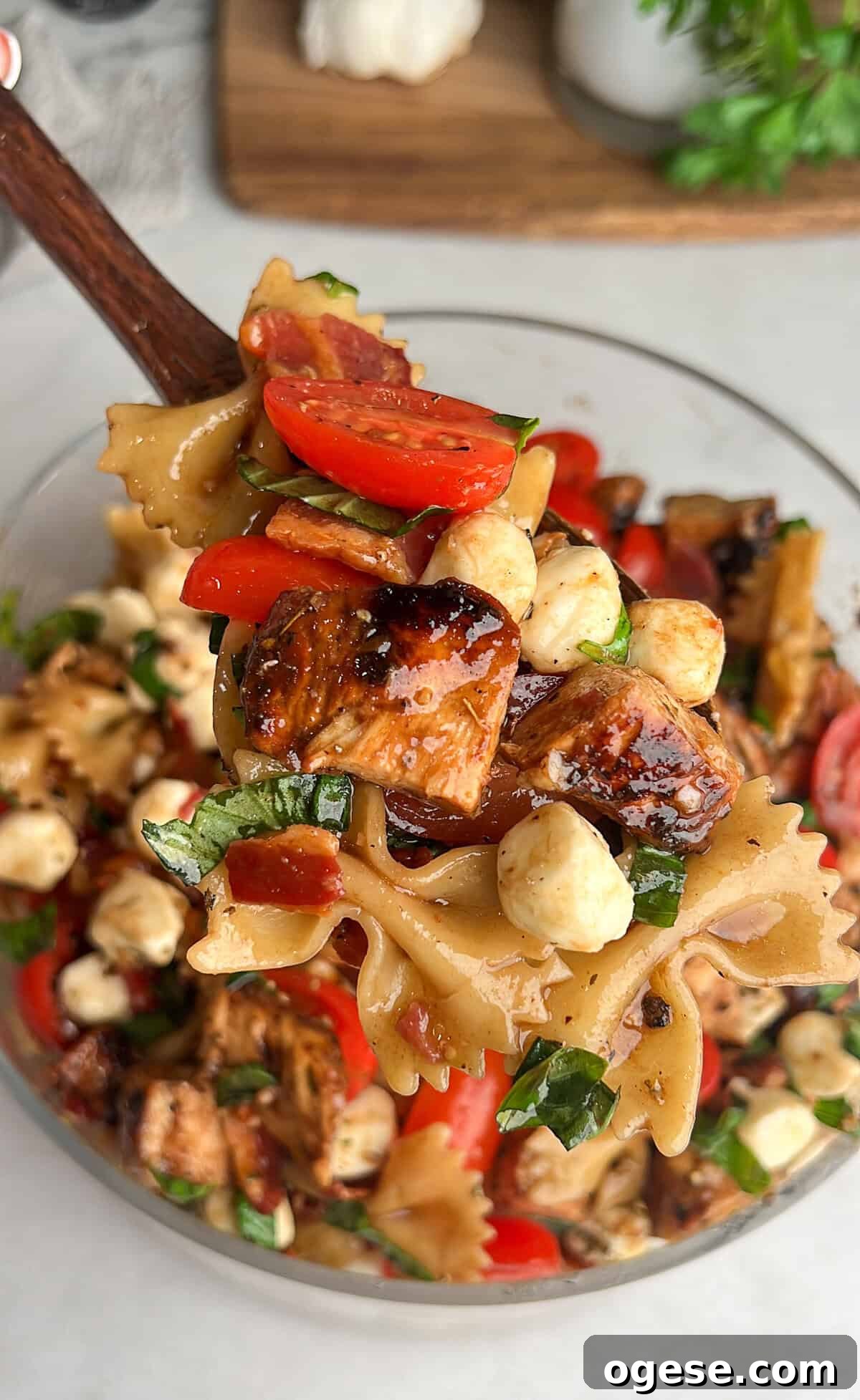 Caprese Pasta Salad is loaded with marinated chicken, tomatoes, mozzarella pearls, bacon, and basil tossed in a tangy balsamic dressing. A spoon serving caprese pasta salad