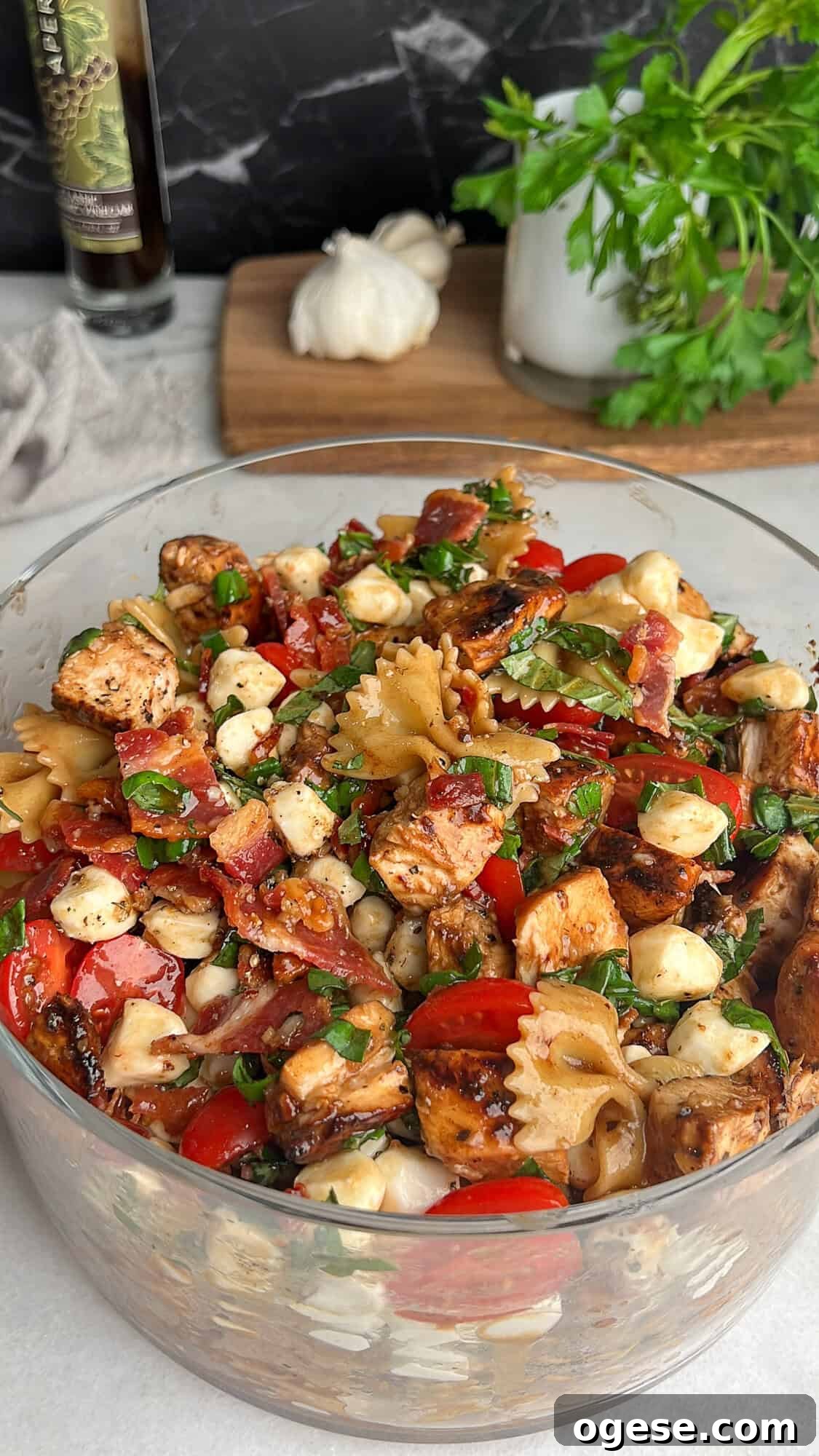 Caprese Pasta Salad is loaded with marinated chicken, tomatoes, mozzarella pearls, bacon, and basil tossed in a tangy balsamic dressing. Caprese pasta salad in a large glass bowl