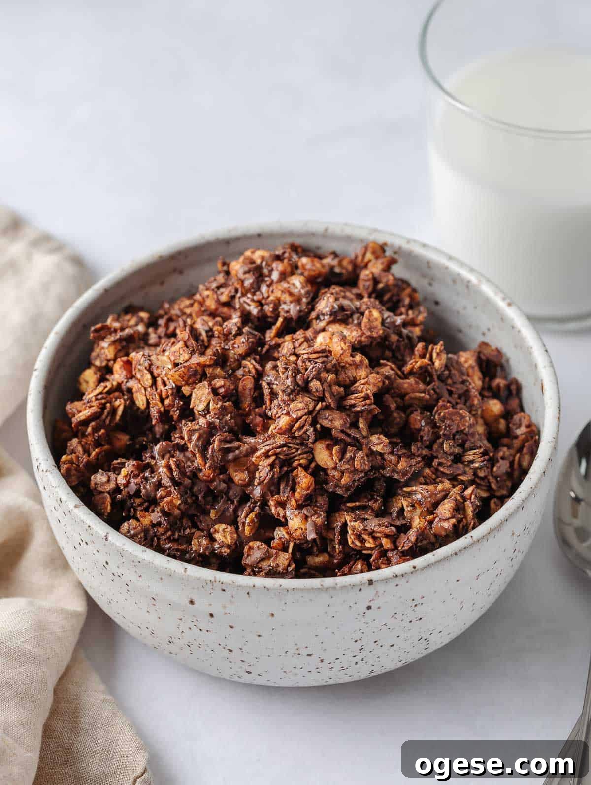 A bowl of chocolate granola with milk in a cup.