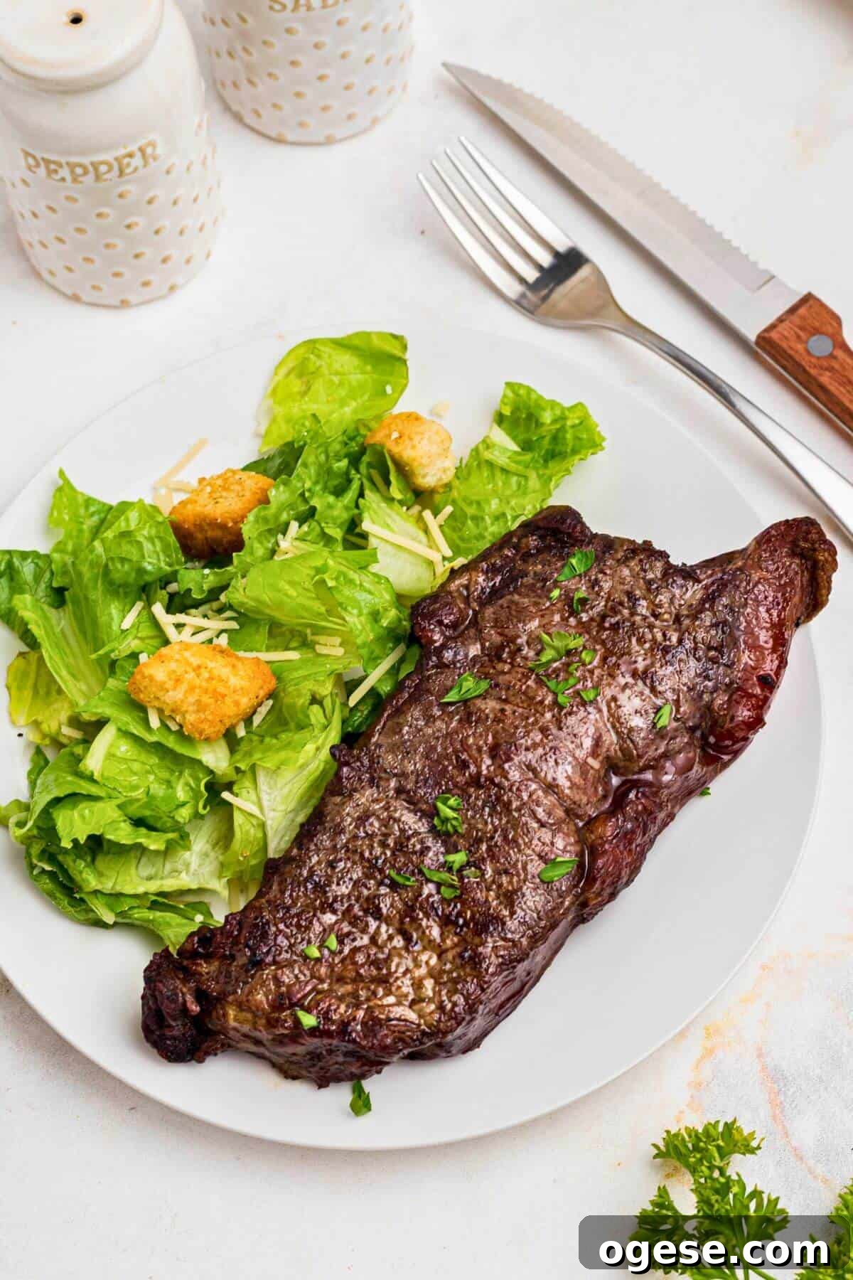 Crispy Air Fryer New York Strip Steak Recipe 2 Air fryer New York strip steak on a plate with salad on the side.
