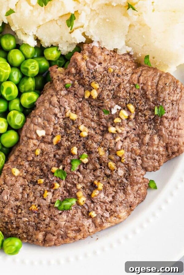 Crispy Air Fryer New York Strip Steak Recipe 11 Air fryer cube steak on a white plate served with green peas and mashed potatoes.