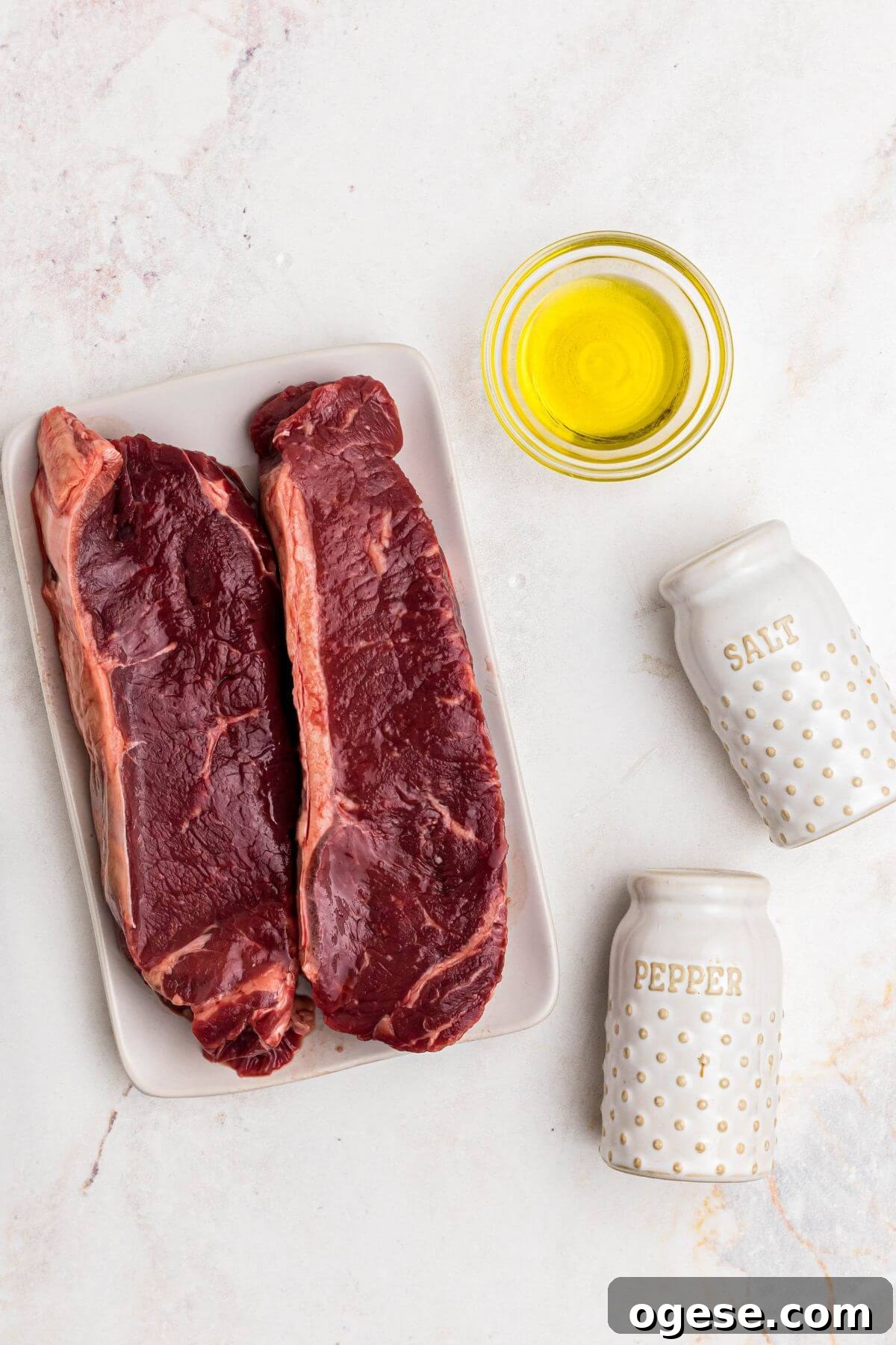 Crispy Air Fryer New York Strip Steak Recipe 4 Uncooked steaks with olive oil and salt and pepper on a marble table.