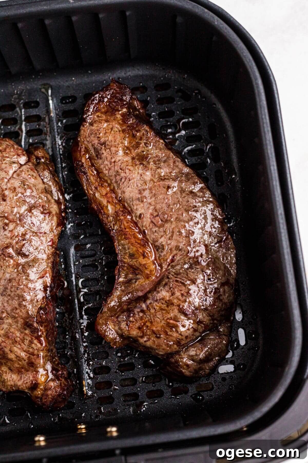 Crispy Air Fryer New York Strip Steak Recipe 7 Juicy cooked New York strip steaks in the air fryer basket after being cooked.