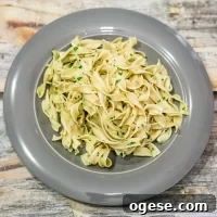 Fettuccine pasta garnished with chopped parsley on a gray plate.