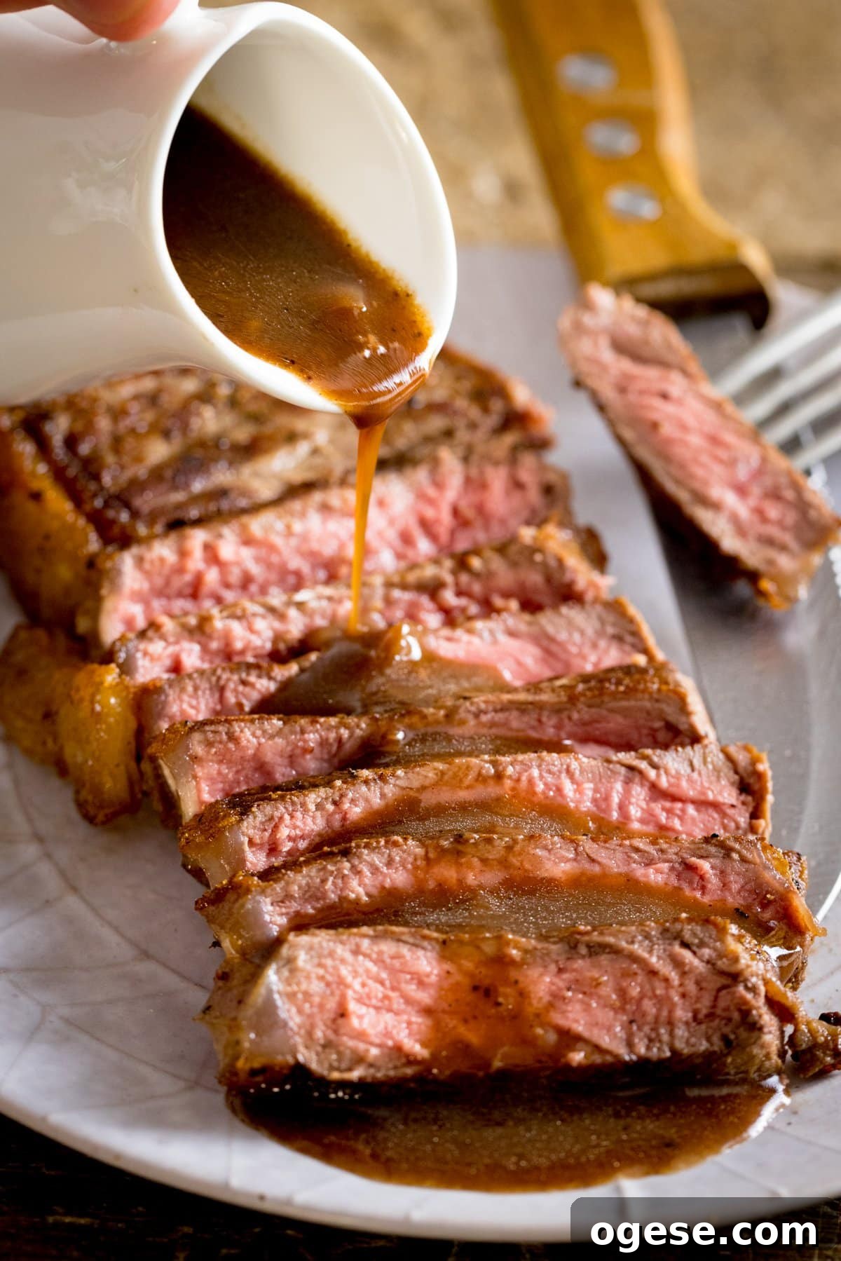 Rich Red Wine Jus Recipe for Steak and Roast 2 A plate of cooked sliced steak with red wine being poured over from a white jug