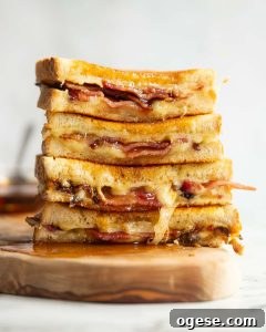 4 bacon grilled cheese halves stacked on each other on wooden board with maple syrup poured over