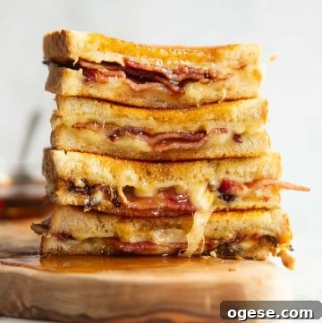 4 bacon grilled cheese halves stacked on each other on wooden board with maple syrup poured over
