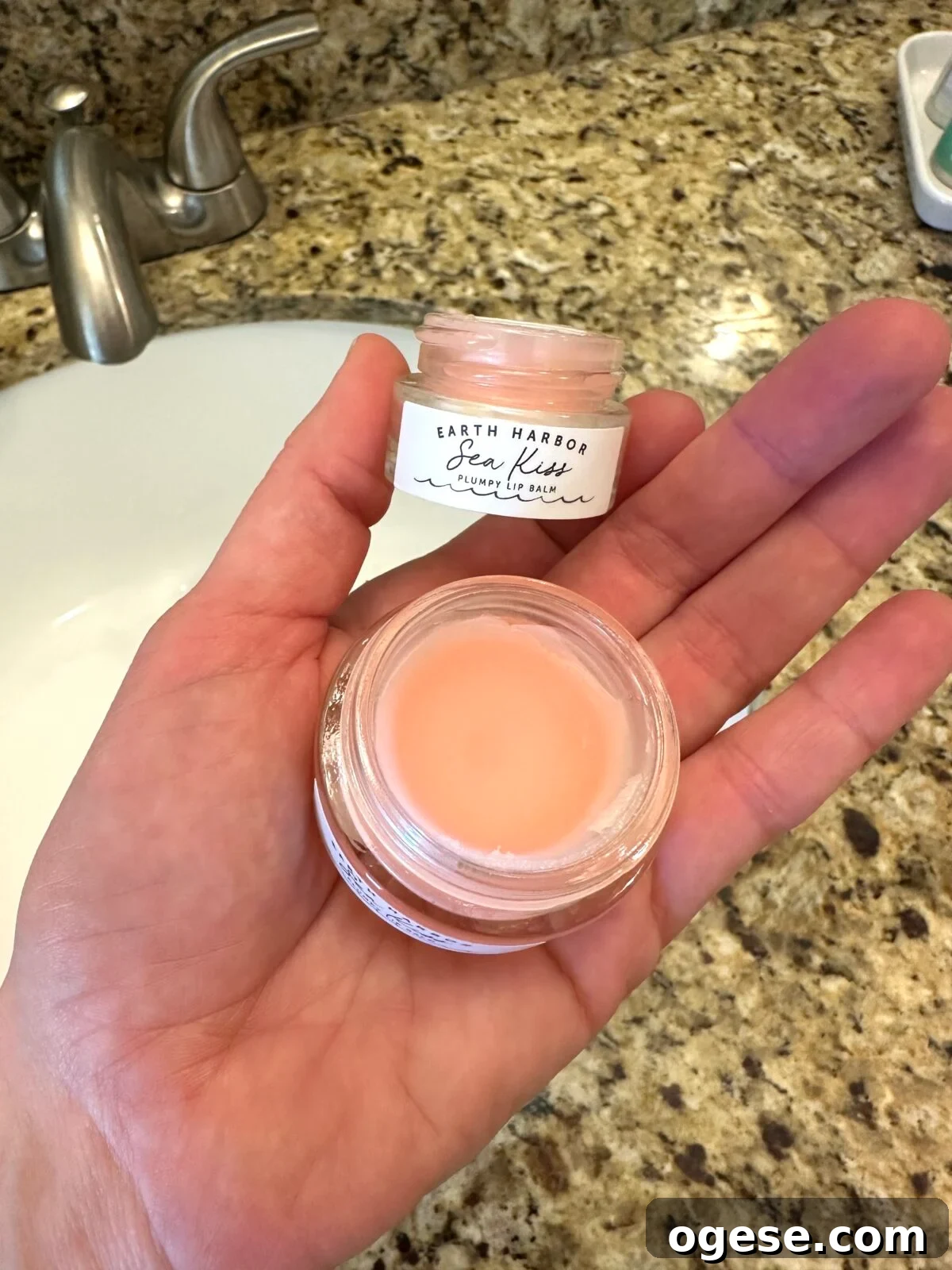 Earth Harbor Skincare Review: Real Pros, Cons, and Results 3 Hand holding open jar of Earth Harbor Sea Kiss Plumpy Lip Balm showing peach-colored product over bathroom sink