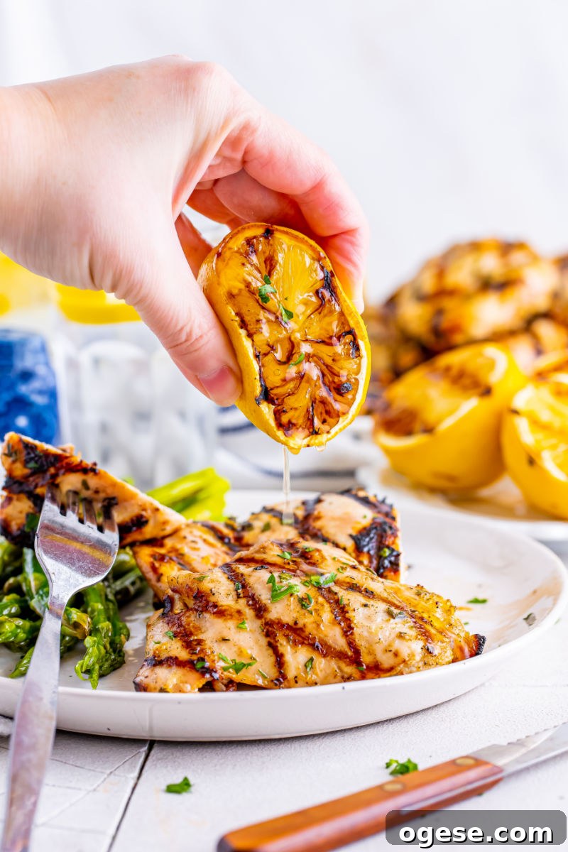 grilled lemon being squeeze over lemon garlic grilled chicken thighs on a plate
