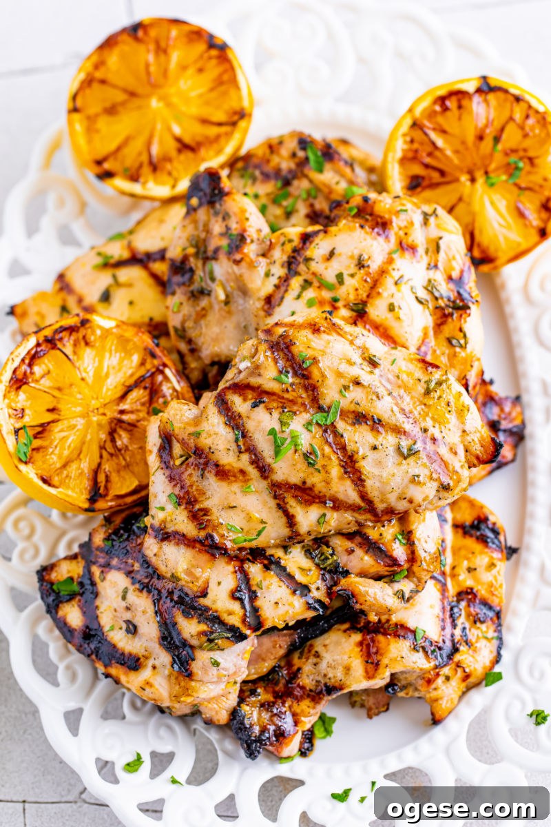lemon garlic grilled chicken thighs piled up on a platter with grilled lemon halves