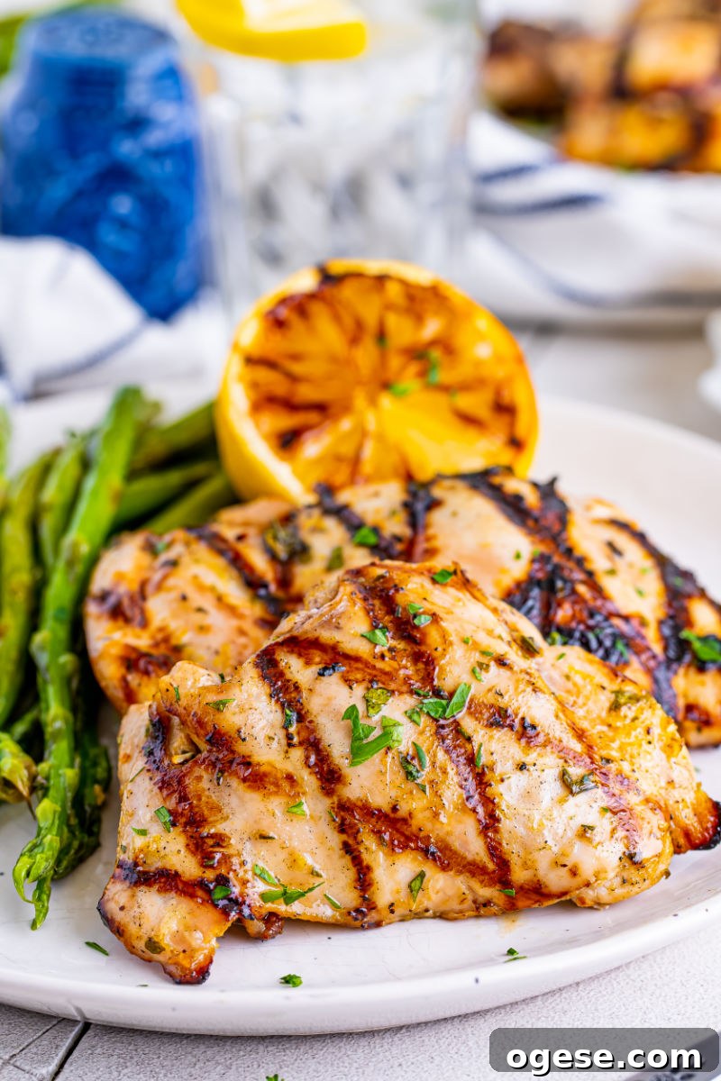 two lemon garlic grilled chicken thighs on a plate with asparagus and a grilled lemon