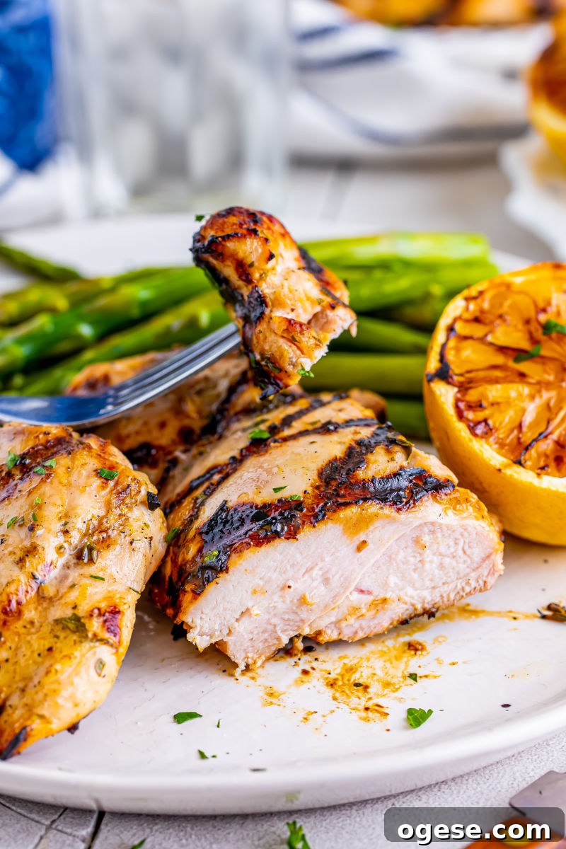 bite of lemon garlic grilled chicken thighs on a fork over the plate of chicken