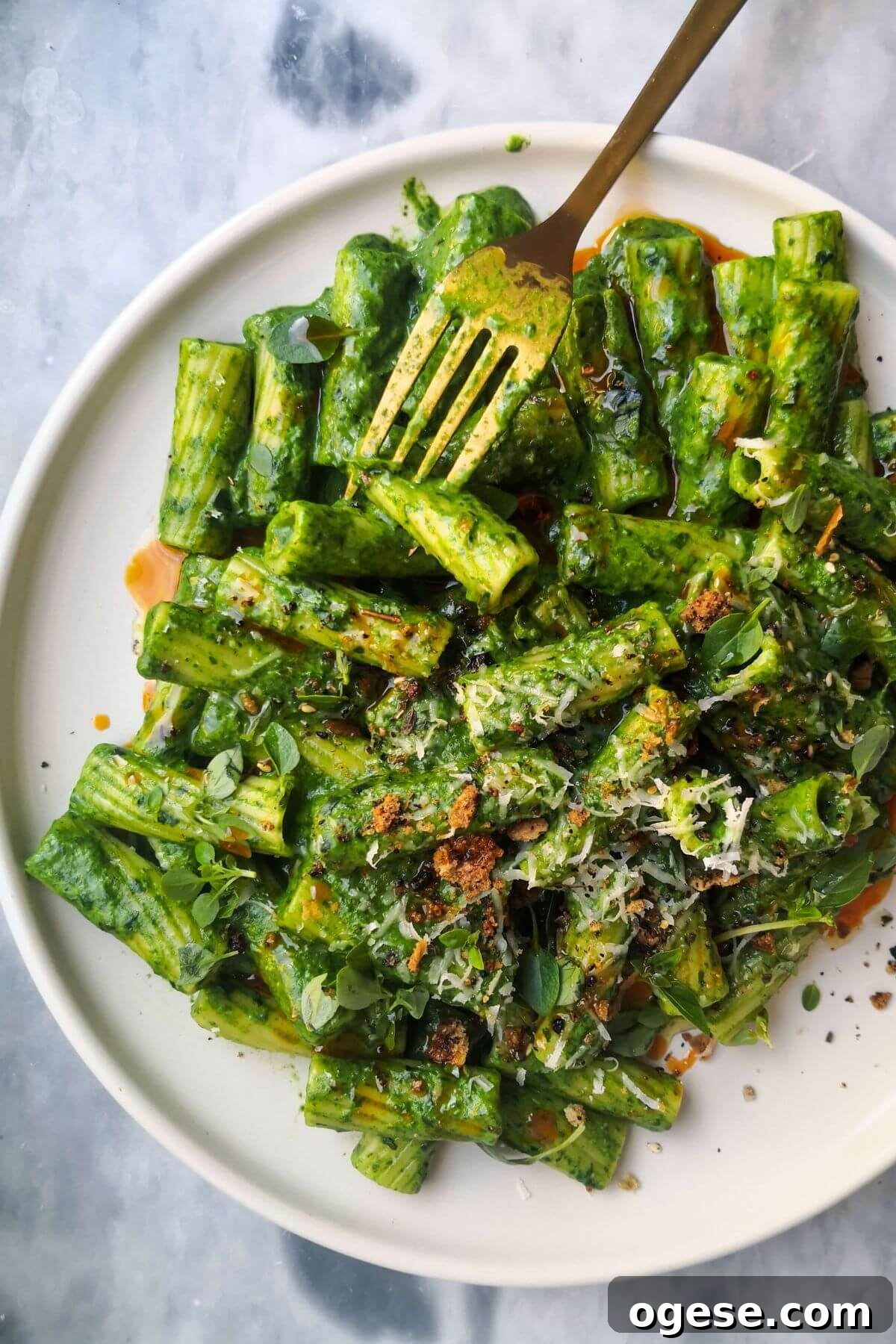 15-Minute Super Green Rigatoni Recipe for Quick Weeknight Dinner 2 Green pasta sauce with rigatoni on a white plate, with gold fork piercing a piece of pasta.