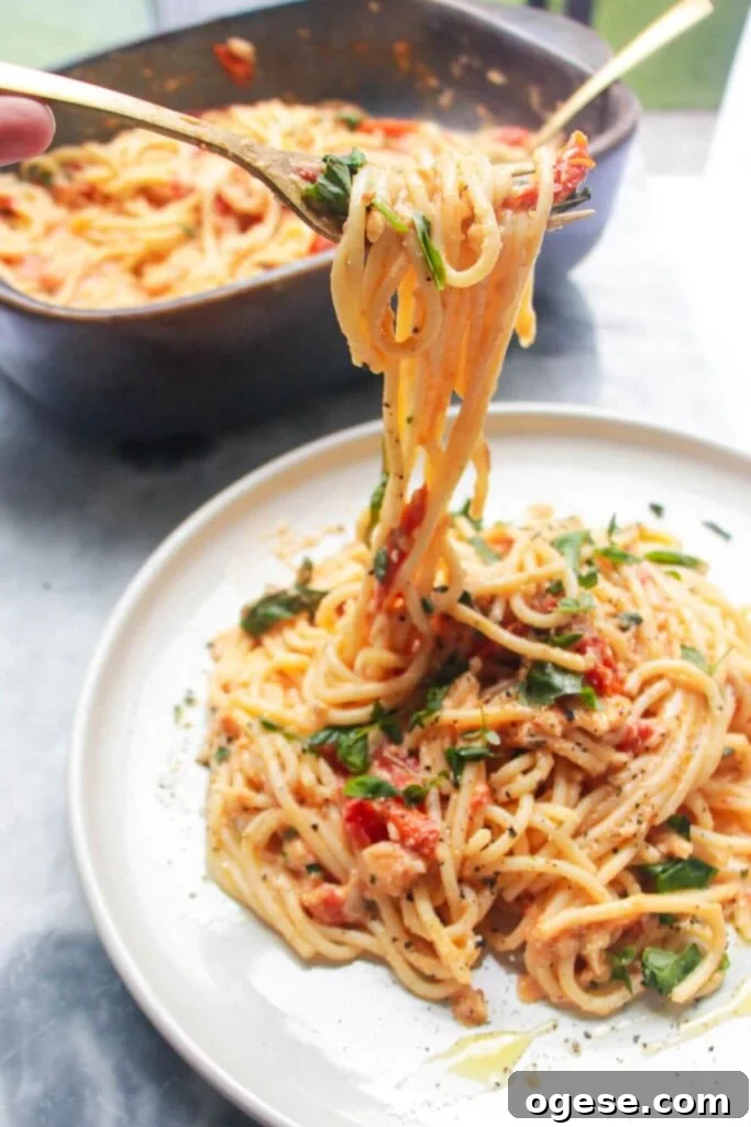 15-Minute Super Green Rigatoni Recipe for Quick Weeknight Dinner 16 A fork pulling up baked burrata and tomato pasta with dish of pasta in the background.