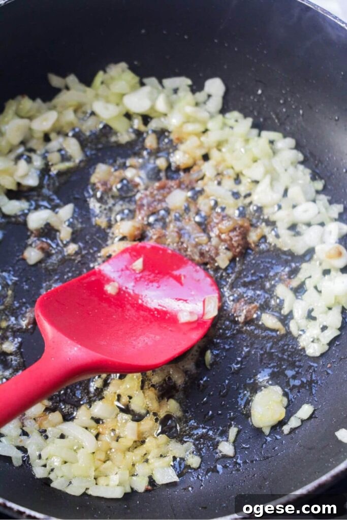 15-Minute Super Green Rigatoni Recipe for Quick Weeknight Dinner 5 Softened onions, garlic and anchovies in a small black pan with a red spatula squashing the anchovies into the oil.