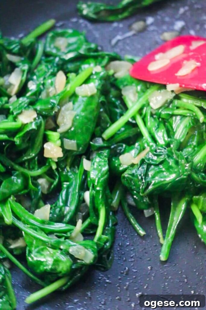 15-Minute Super Green Rigatoni Recipe for Quick Weeknight Dinner 7 Wilting spinach being stirred in a black pan with a red spatula.