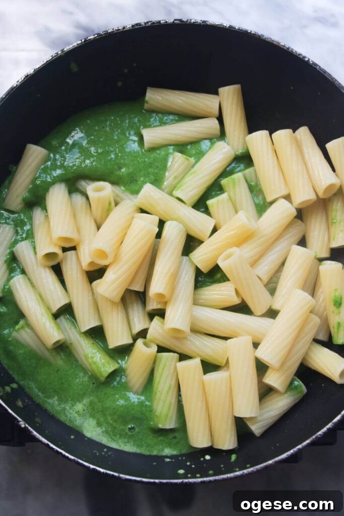 15-Minute Super Green Rigatoni Recipe for Quick Weeknight Dinner 10 Rigatoni being added to a small black pan with green sauce in it.