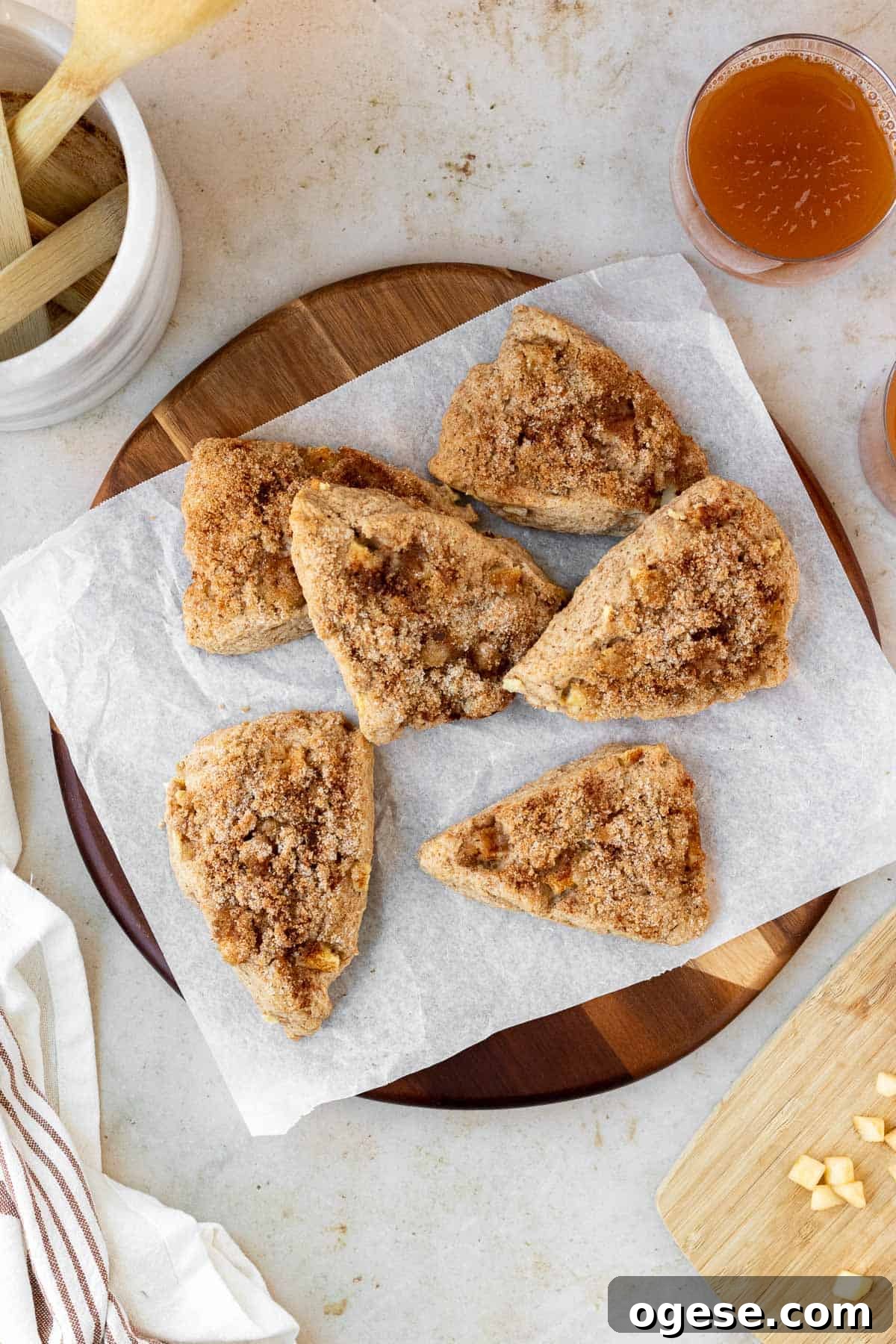 Apple Cinnamon Scones with Crunchy Cinnamon Topping 2 apple cinnamon scones sit atop a parchment lined round wood cutting board