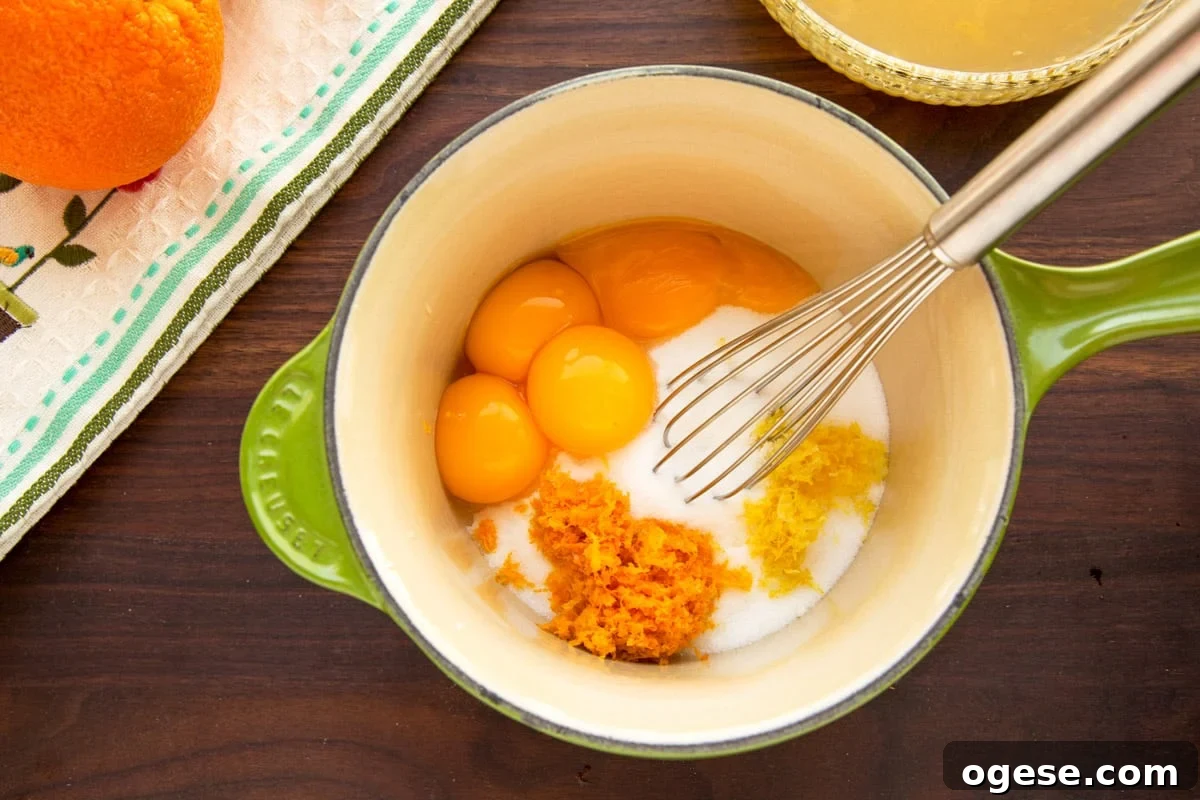 egg yolks, sugar, and citrus zest in a green and white saucepan with a stainless steel whisk
