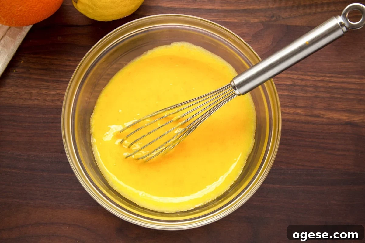 orange curd in a glass bowl with a stainless steel whisk on a dark wood cutting board