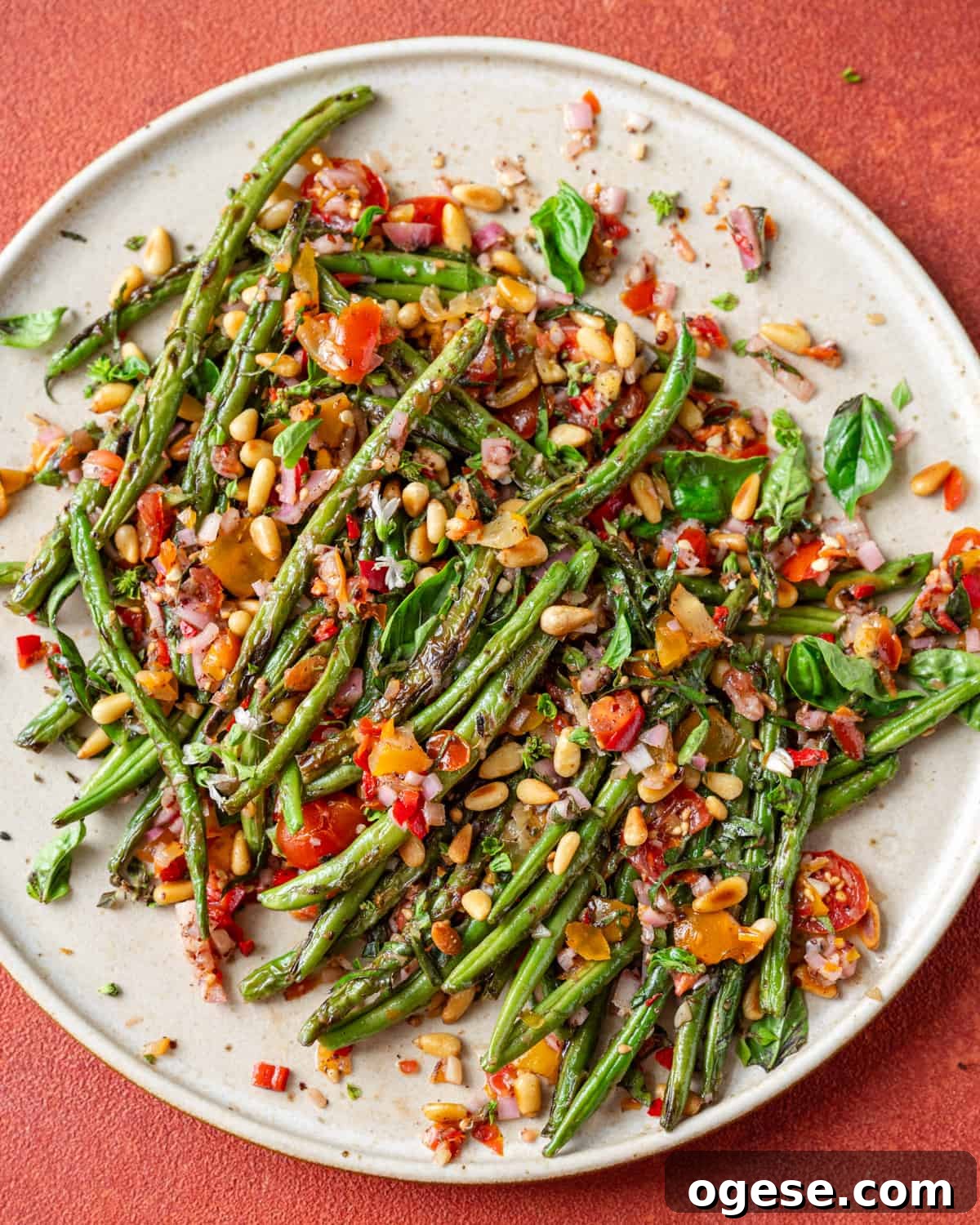 Overhead view of plate of charred green beans on a red table.