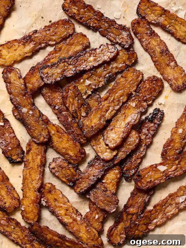 Crispy browned tempeh bacon slices on a piece of parchment paper.