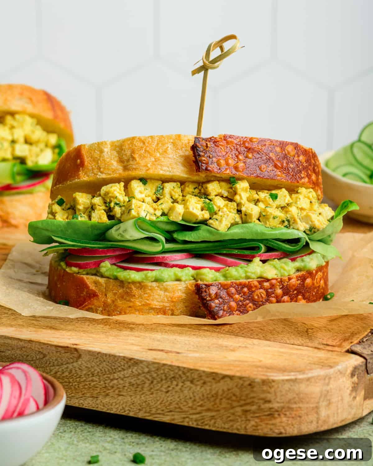 Side view of vegan egg salad sandwich on a wooden cutting board.