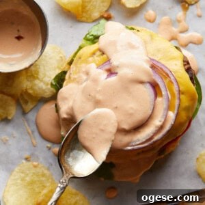 Creamy Burger Sauce Recipe Without Pickles or Relish 6 Gold spoon spreading burger sauce onto a burger.