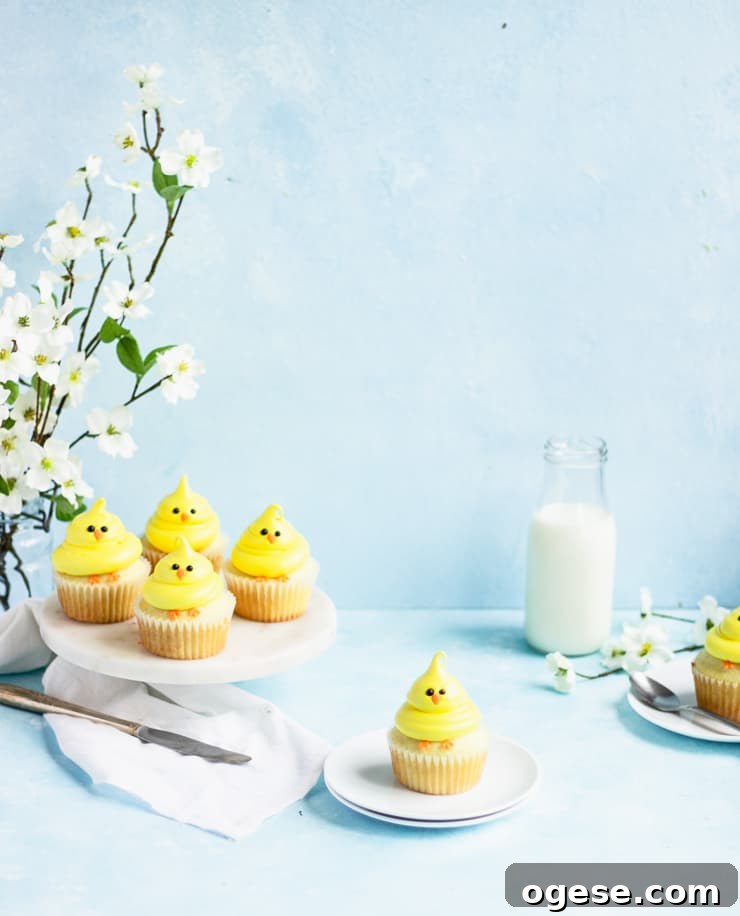 Chick cupcake on a plate with a platter of cupcakes, a vase of flowers and a bottle of milk in the background