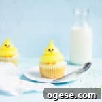 Chick cupcake on a plate with a spoon. A glass of milk is in the background with sprinkles strewn around the sides.