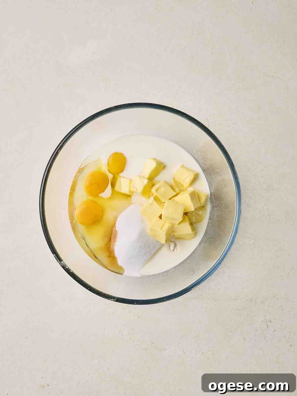 Cubes of butter, eggs, sugar and flour in a glass bowl.