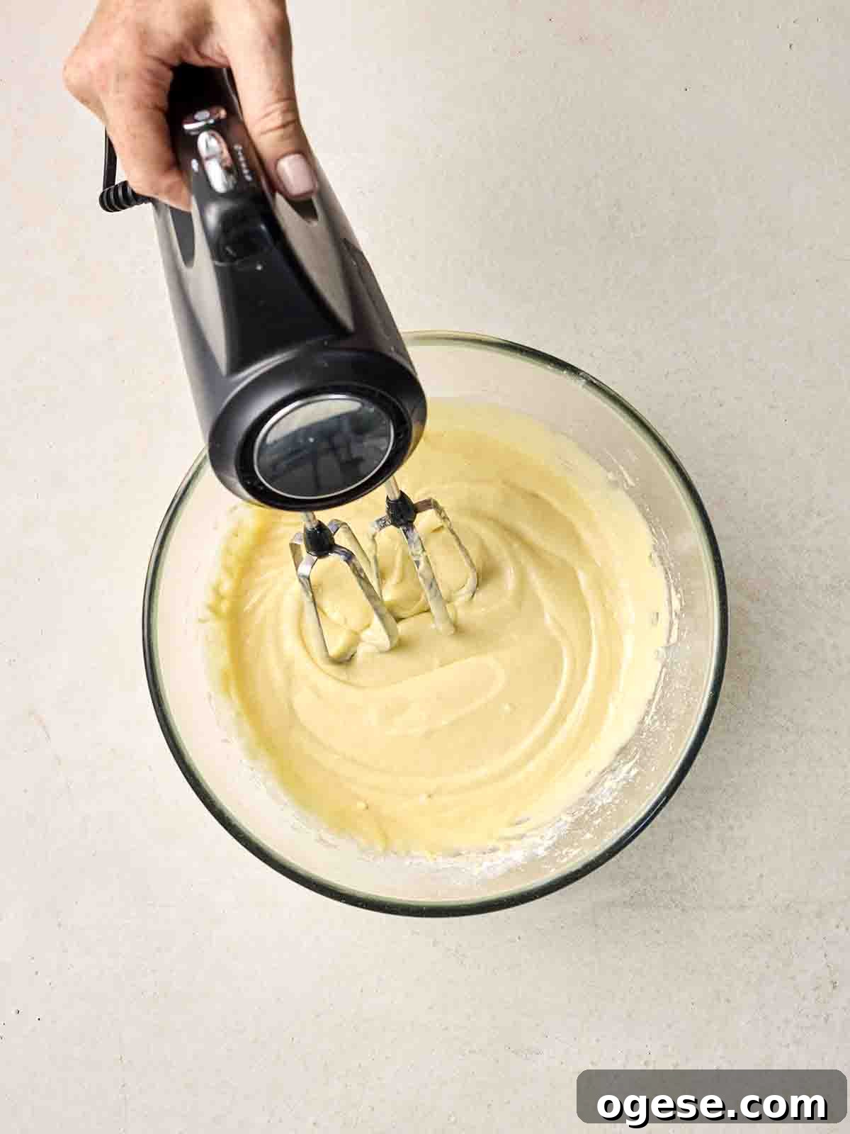 Cake batter in a glass bowl being mixed together with an electric whisk.