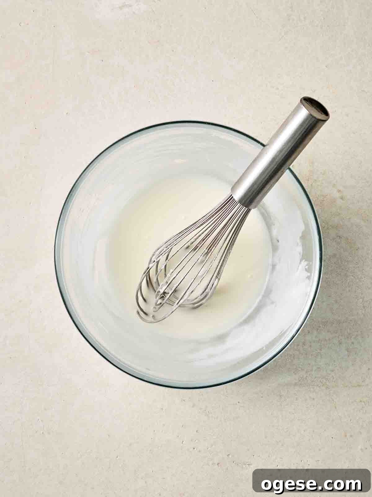 A glass bowl filled with icing and a whisk.
