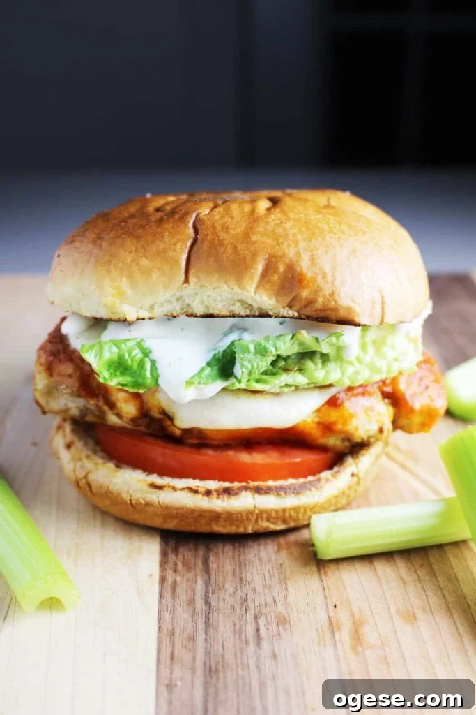 A Buffalo chicken burger topped with ranch dressing, tomato and lettuce on a wooden cutting board