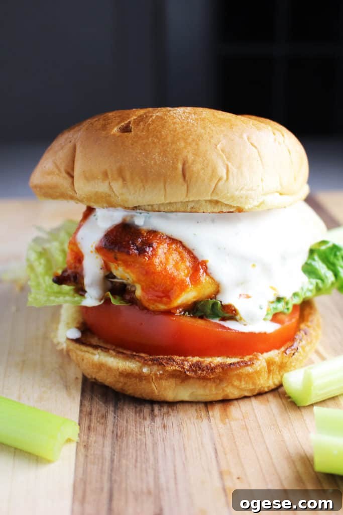 A Buffalo chicken burger with cheese, ranch, tomato and lettuce on a wooden cutting board