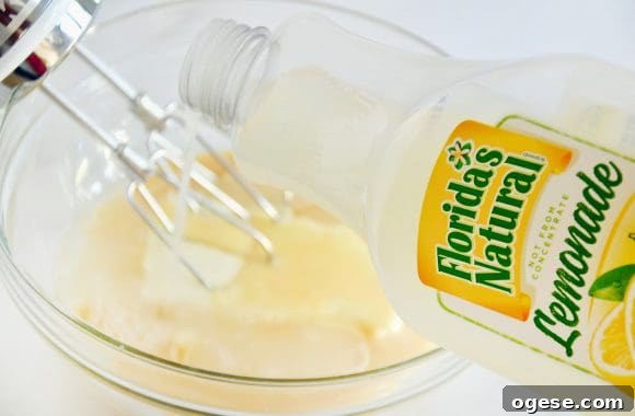 A bottle of lemonade being poured into a clear bowl containing cream cheese