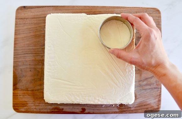 A wood cutting board containing a sheet of ice cream being cut out with a circular cookie cutter