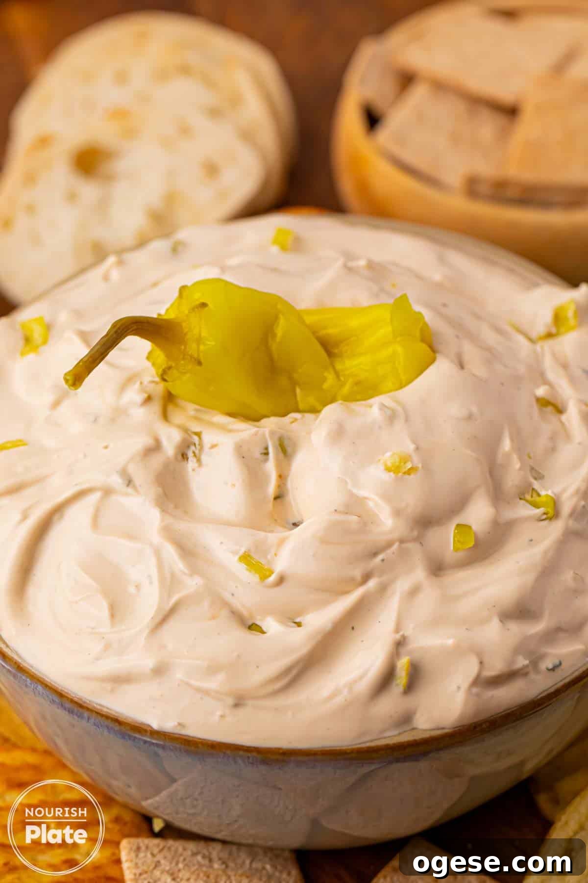 Mississippi Sin Dip in a serving bowl topped with a whole pepperoncini, with crackers and bread in the background