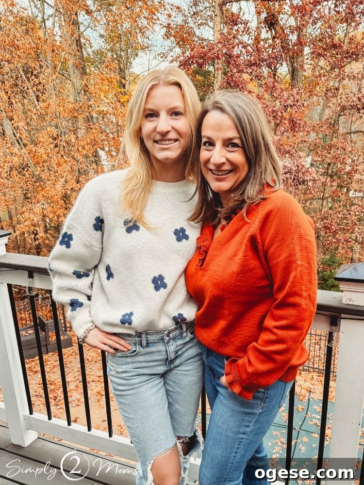 Anne from simply2moms with one of her daughters standing on a deck with fall trees.
