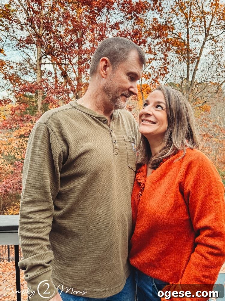 Anne from Simply2Moms with her husband standing outside with fall foliage behind them.