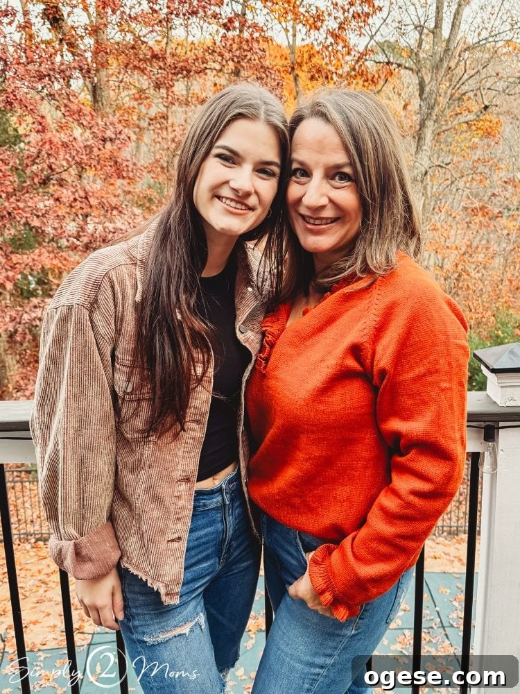 Anne from simply2moms with one of her daughters standing on a deck with fall colors on the trees.