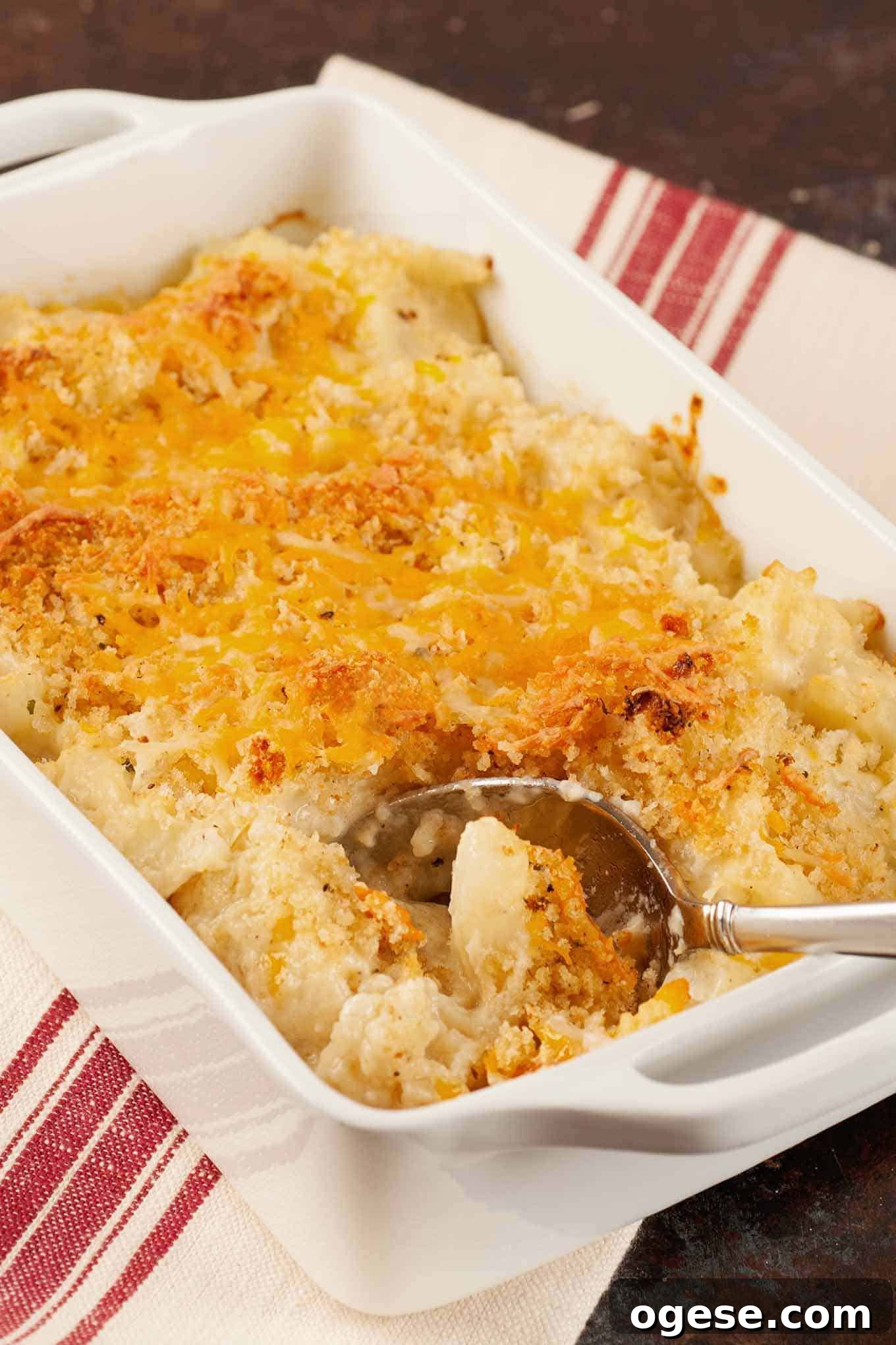 Golden brown roasted cauliflower gratin topped with melted cheddar cheese and crispy breadcrumbs in a white baking dish with serving spoon.